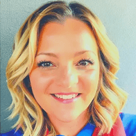 Headshot of a smiling woman with blonde, wavy shoulder-length hair, wearing a blue top with a red accent.